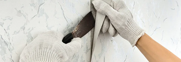 Person entfernt Tapete mit Spachtel